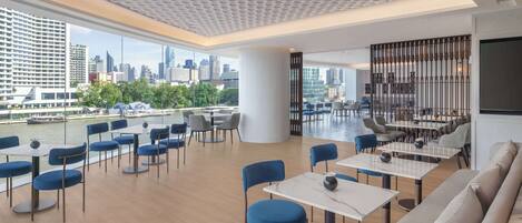 A modern dining area with tables and chairs, a large window with a city view, and a decorative ceiling.