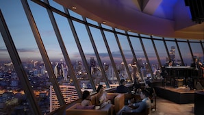 Ein Hochhaus mit weiter Aussicht auf die Stadt, einem Klavier und einer Gruppe von Menschen, die in einer Lounge sitzen.