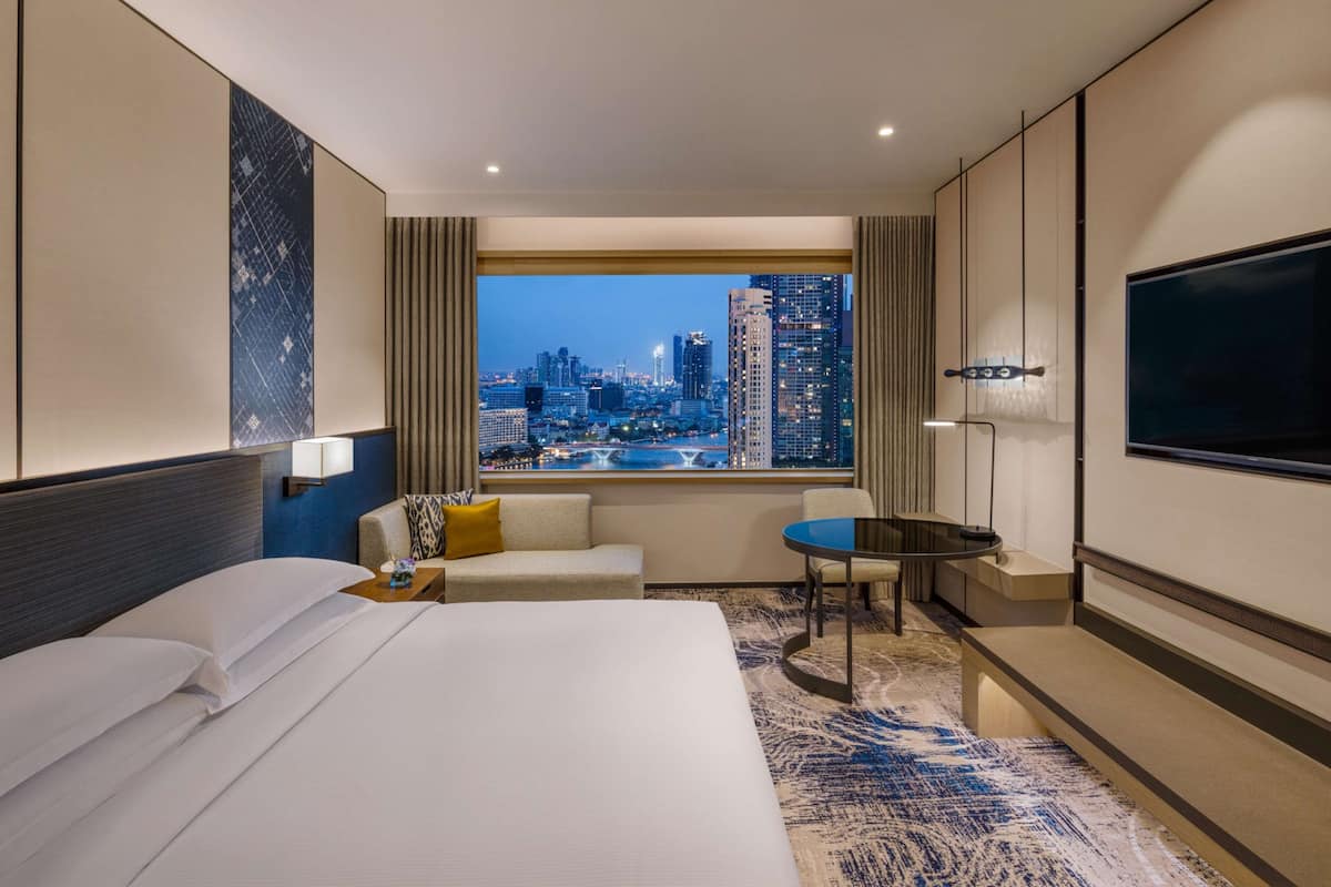 Una habitación de hotel con una cama grande, un sofá, una mesita, un televisor y vistas a un horizonte urbano.