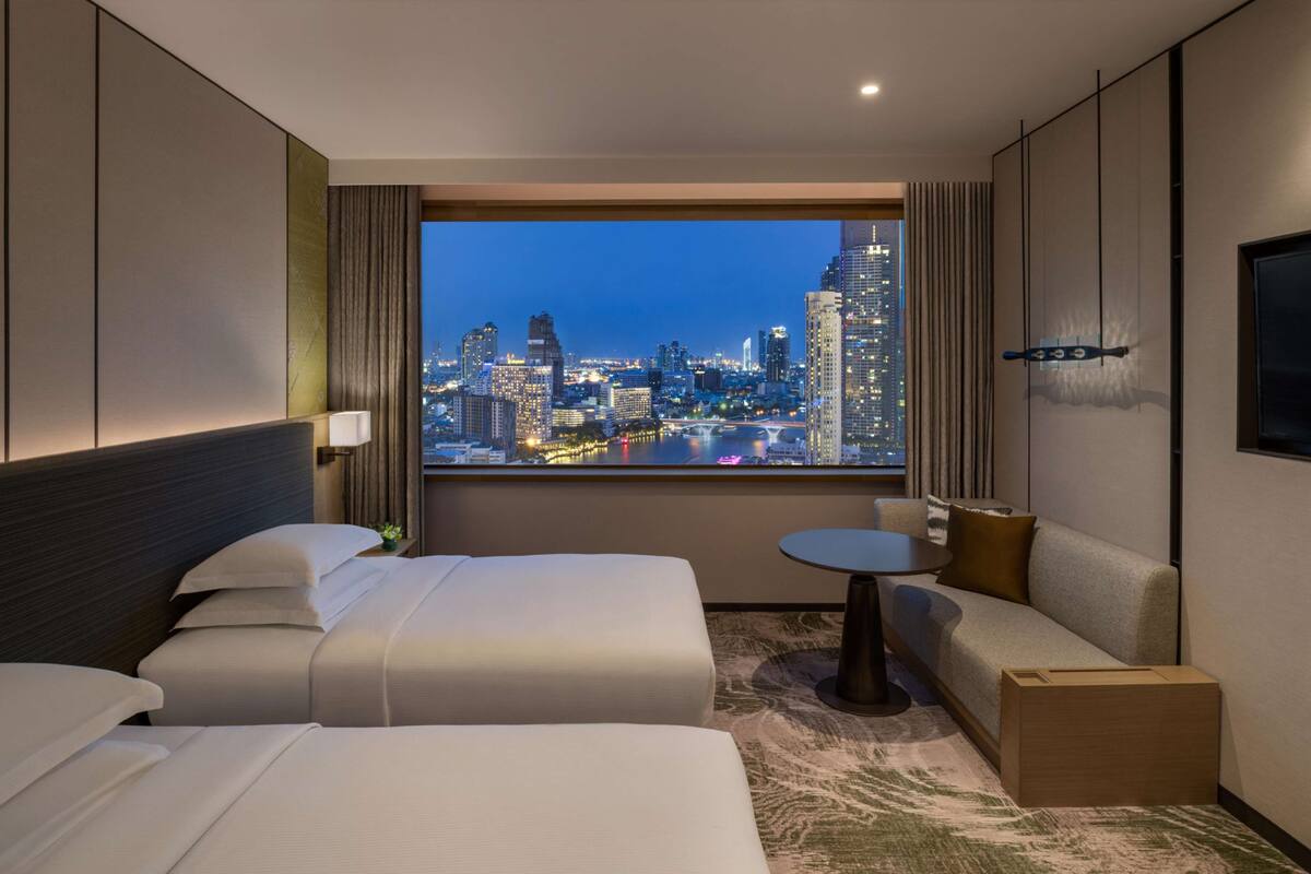 Habitación de hotel con dos camas, un sofá, una mesita y vistas a la ciudad.