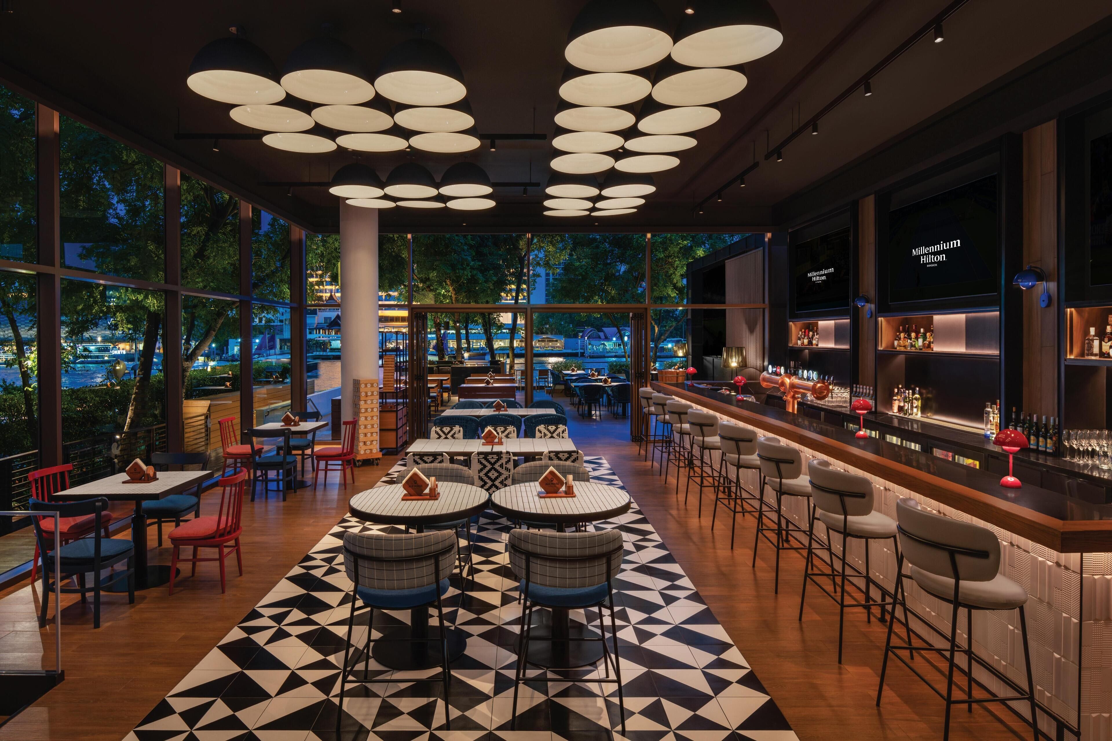 Een moderne bar met een lange toonbank, barstoelen en een groot scherm waarop de naam van het hotel staat.