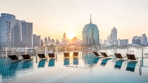 Ein Fernblick auf eine Skyline im Sonnenuntergang, begleitet von einem Infinity-Pool und Liegestühlen.