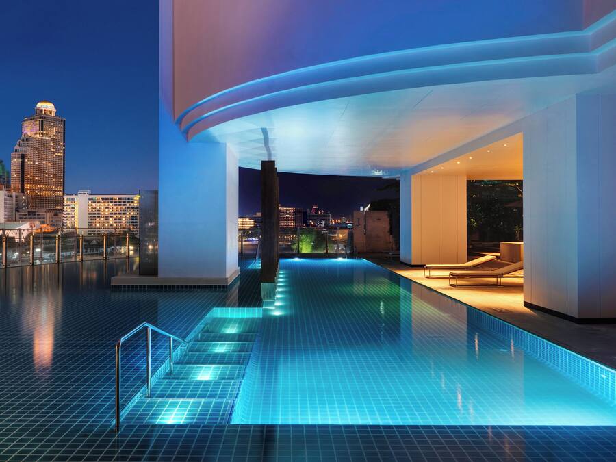 A rooftop infinity pool with a city view, modern architecture, and lounge area.