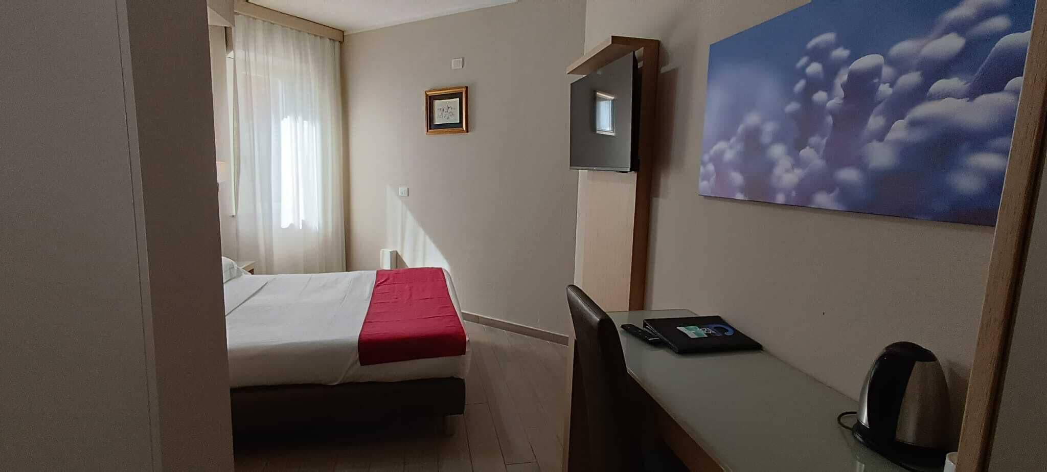 Une chambre d’hôtel avec un lit, un bureau, une chaise, une télévision et un tableau au mur.