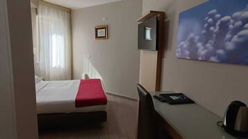 Une chambre d’hôtel avec un lit, un bureau, une chaise, une télévision et un tableau au mur.