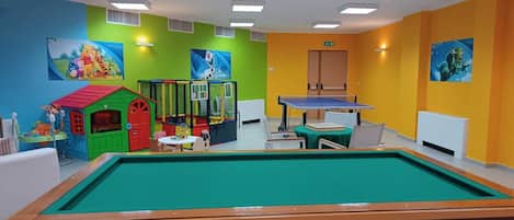 A children's play area with a pool table, colorful play structures, and cartoon-themed wall decorations.