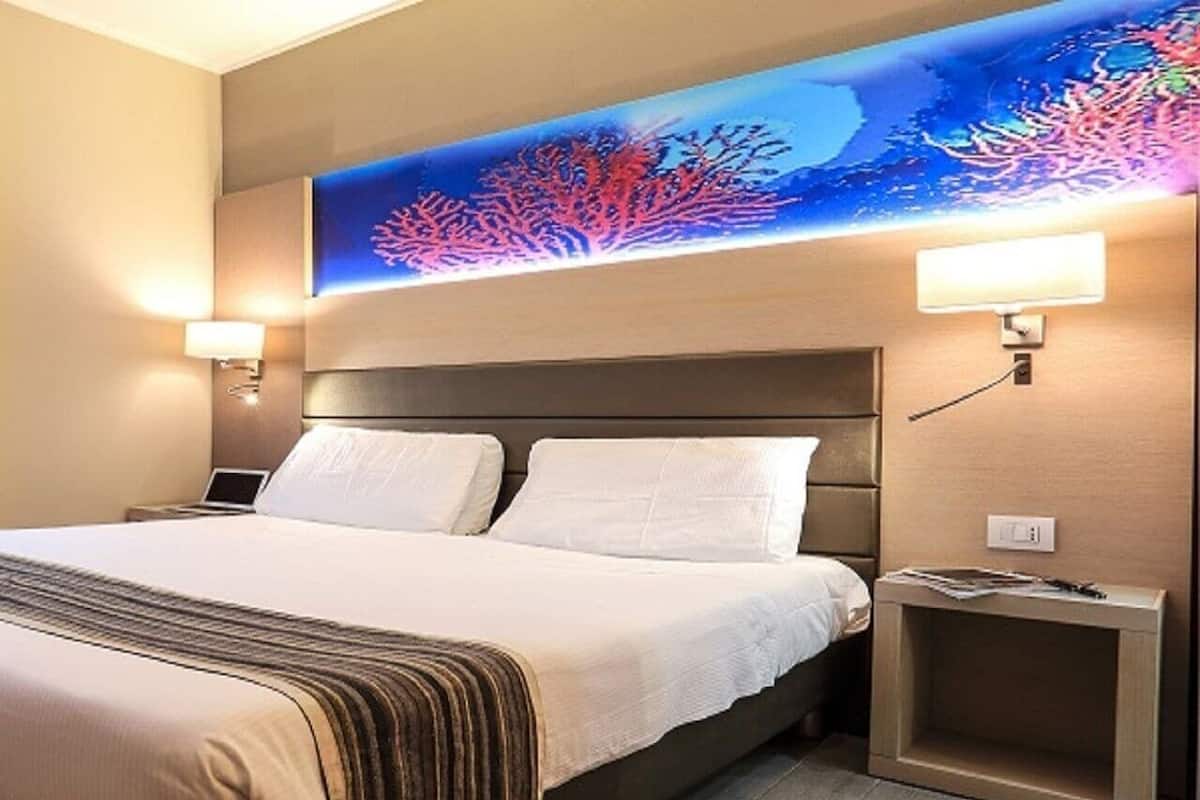 Ein Hotelzimmer mit einem Bett, zwei Nachttischlampen, einem Nachttisch und einem Wandbild.