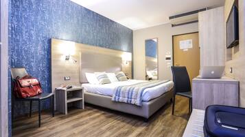 Quarto de hotel moderno com uma cama grande, uma escrivaninha com um laptop, uma cadeira, uma bolsa vermelha e piso de madeira.