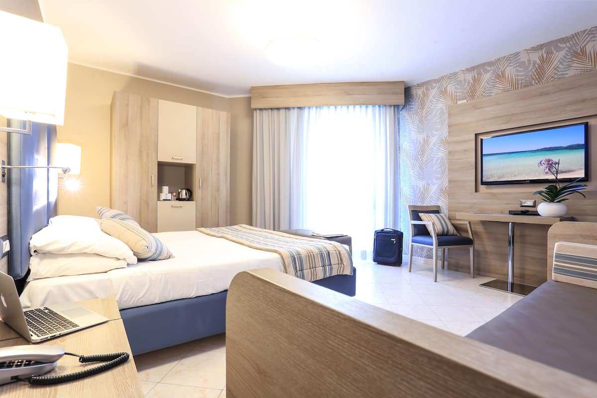 Ein Hotelzimmer mit Bett, Schreibtisch, Stuhl, Fernseher und einem Fenster mit Vorhängen.