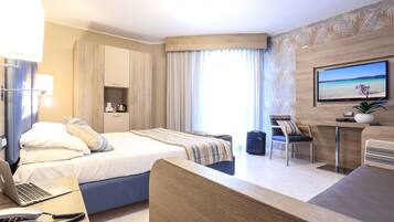 Habitación de hotel con cama, escritorio, silla, televisor y ventana con cortinas.