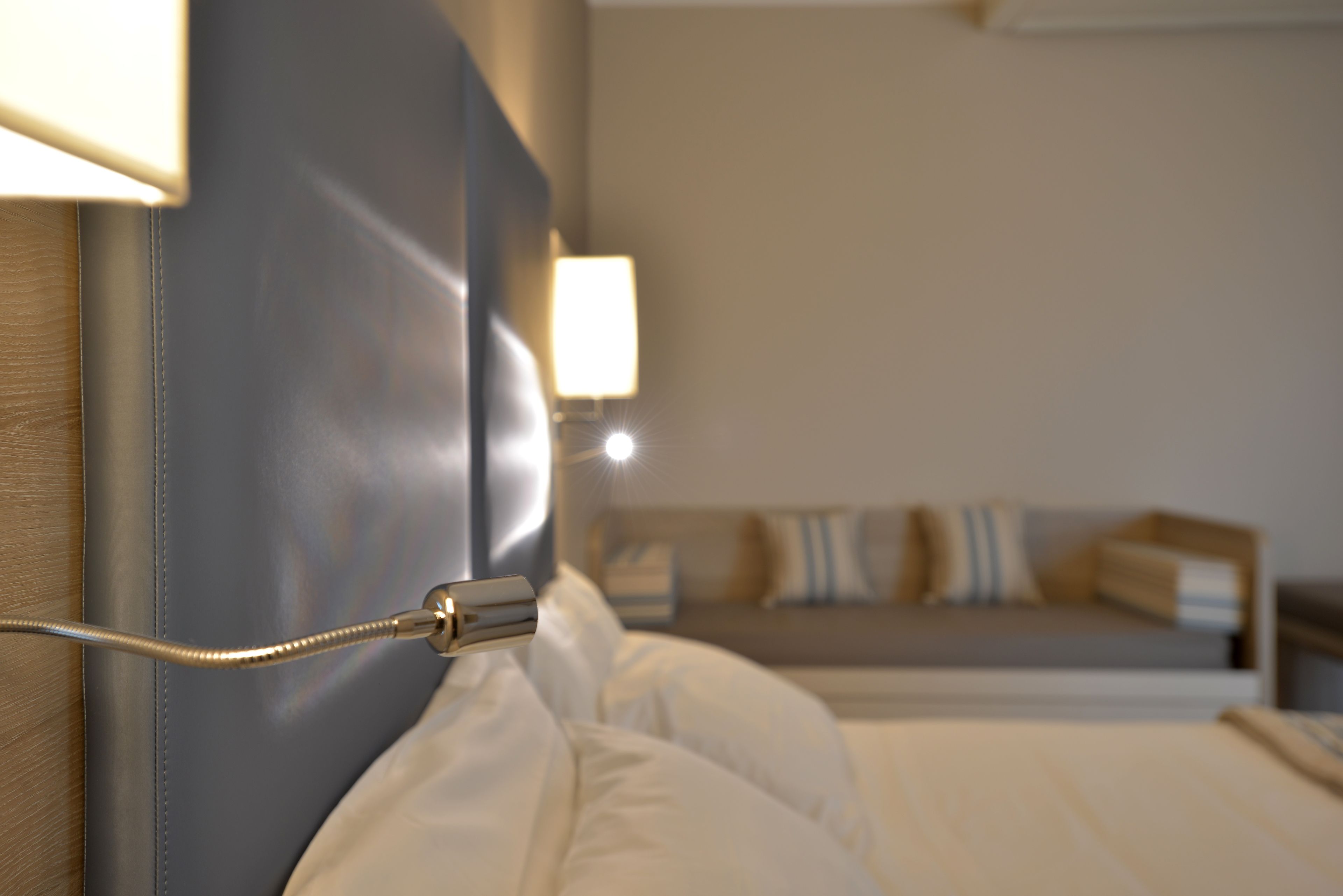 Una camera d'albergo con un letto, una testiera e una lampada da comodino.