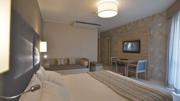 Quarto de hotel com uma cama grande, uma escrivaninha com cadeira, televisão e um sofá.