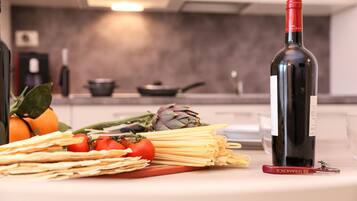 Una encimera de cocina con una botella de vino tinto, pasta, tomates, alcachofas y un sacacorchos.