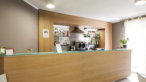 A bar area with a wooden counter, shelves of liquor bottles, a coffee machine, and a potted plant. - Alma Di Alghero Hotel (Alghero)