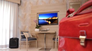 A hotel room with a bed, a desk, a chair, a television, and a red bag. - Alma Di Alghero Hotel (Alghero)