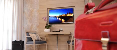 A hotel room with a bed, a desk, a chair, a television, and a red bag.