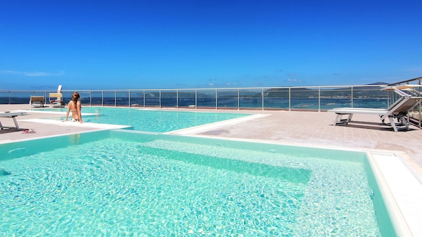 A rooftop pool with clear blue water, sun loungers, and a view of the ocean. - Alma Di Alghero Hotel (Alghero)