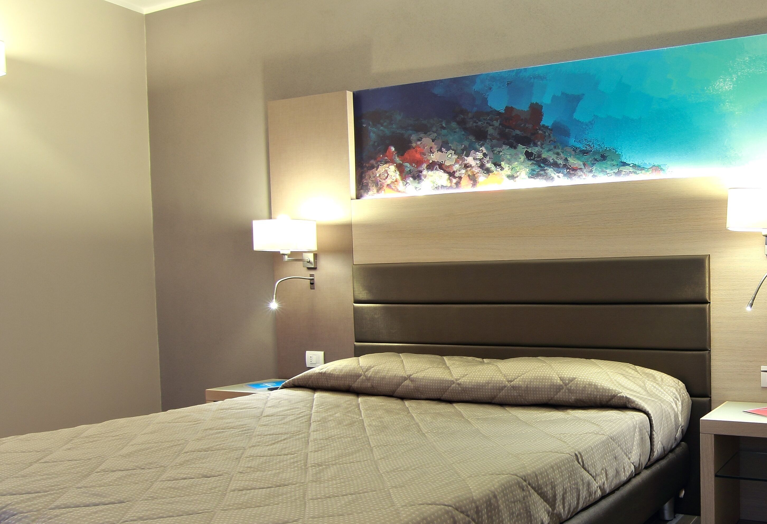 Une chambre d’hôtel avec un lit, une table de chevet, une lampe fixée au mur et un grand tableau représentant une scène sous-marine.