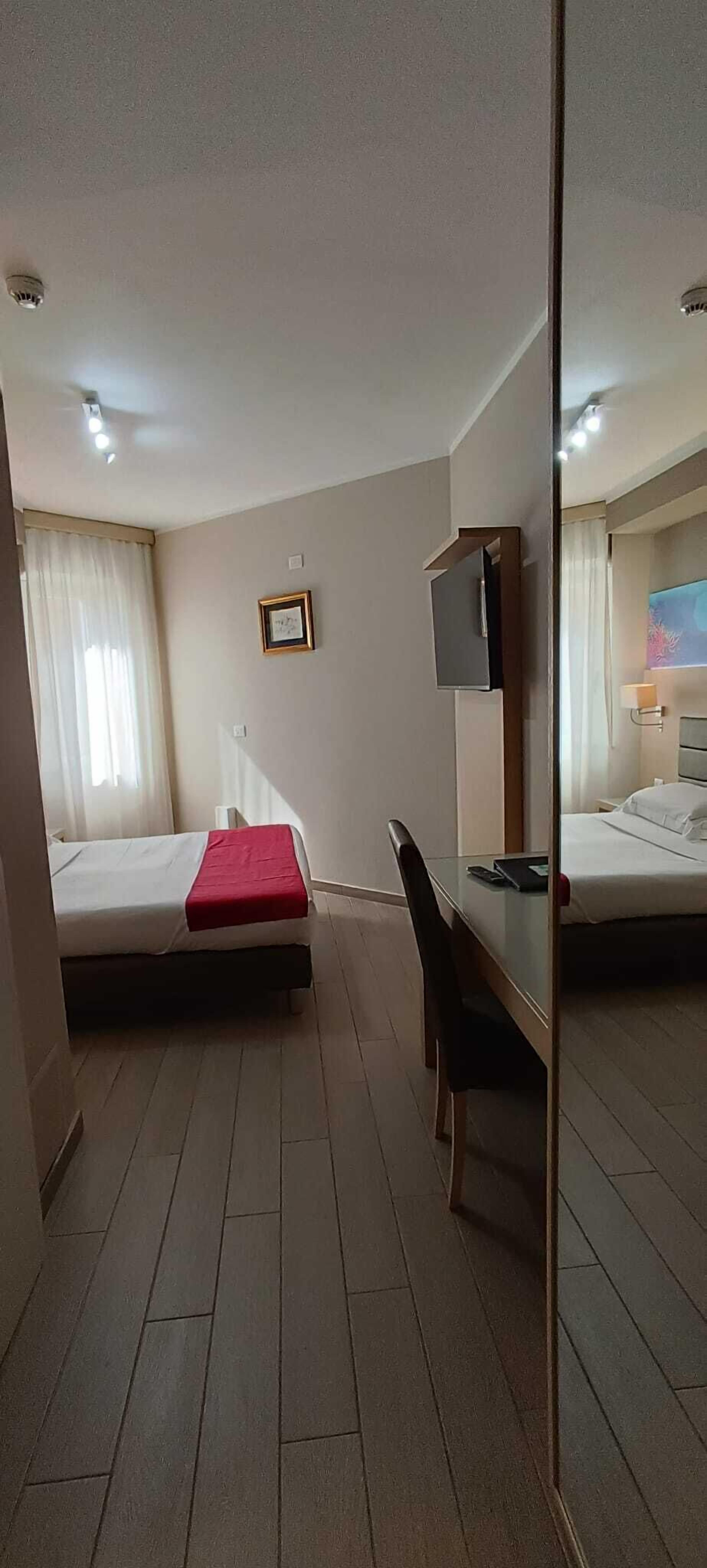 A hotel room with two beds, a desk, a chair, a TV, and a mirror.