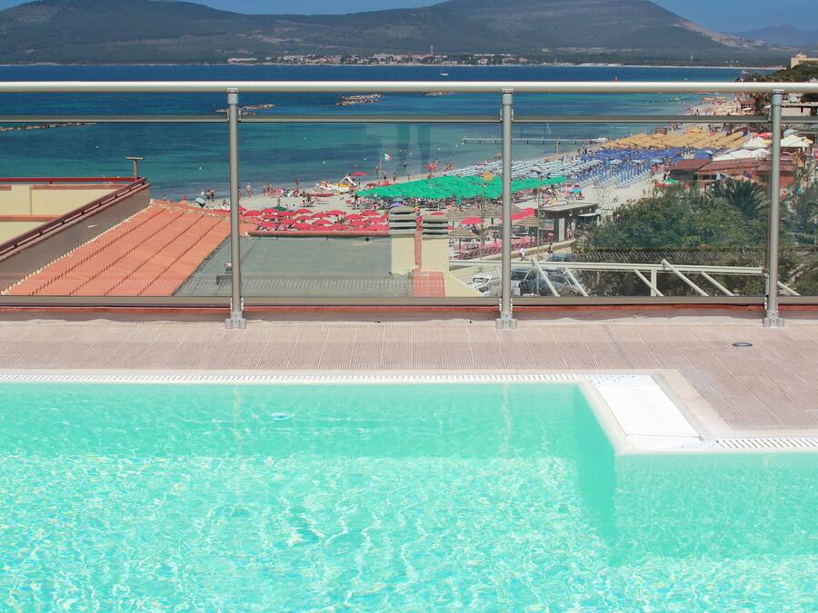 Una piscina con agua cristalina, una playa con sombrillas y vistas al mar y las montañas.