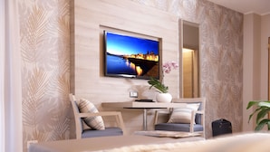 A hotel room with a bed, a desk with a chair, a television mounted on the wall, and a potted plant. - Alma Di Alghero Hotel (Alghero)