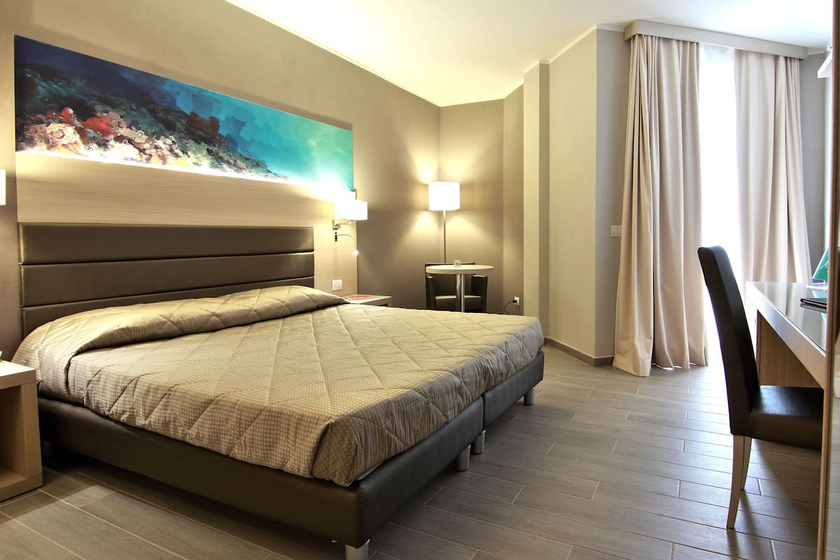 Ein Hotelzimmer mit Bett, Schreibtisch, Stuhl, Lampe und einem Bild an der Wand.