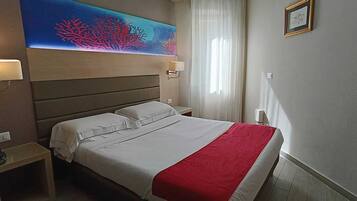 A hotel room with a bed, a nightstand, a lamp, a painting, and a window with curtains.