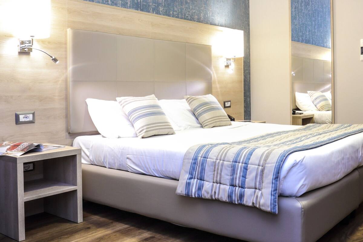 Ein modernes Hotelzimmer mit einem großen Bett, einem Nachttisch, einem Spiegel und einer Wandleuchte.