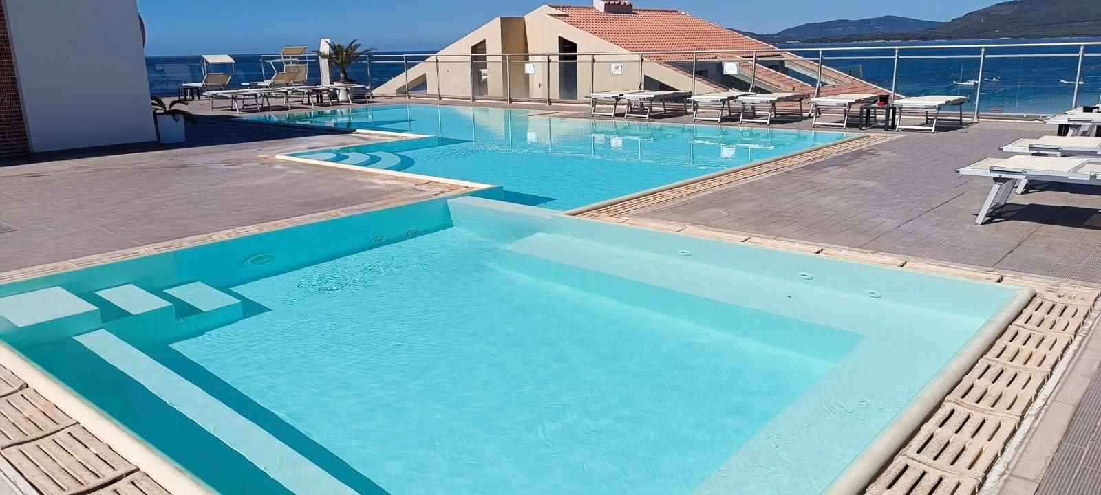 A rooftop pool with clear blue water, lounge chairs, and a view of the sea.