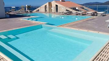 A rooftop pool with clear blue water, lounge chairs, and a view of the sea.