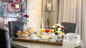 A breakfast tray with pastries, coffee, juice, and flowers on a table in a room with patterned wallpaper and a vase of flowers. - Zaki Hotel  (Meknes)