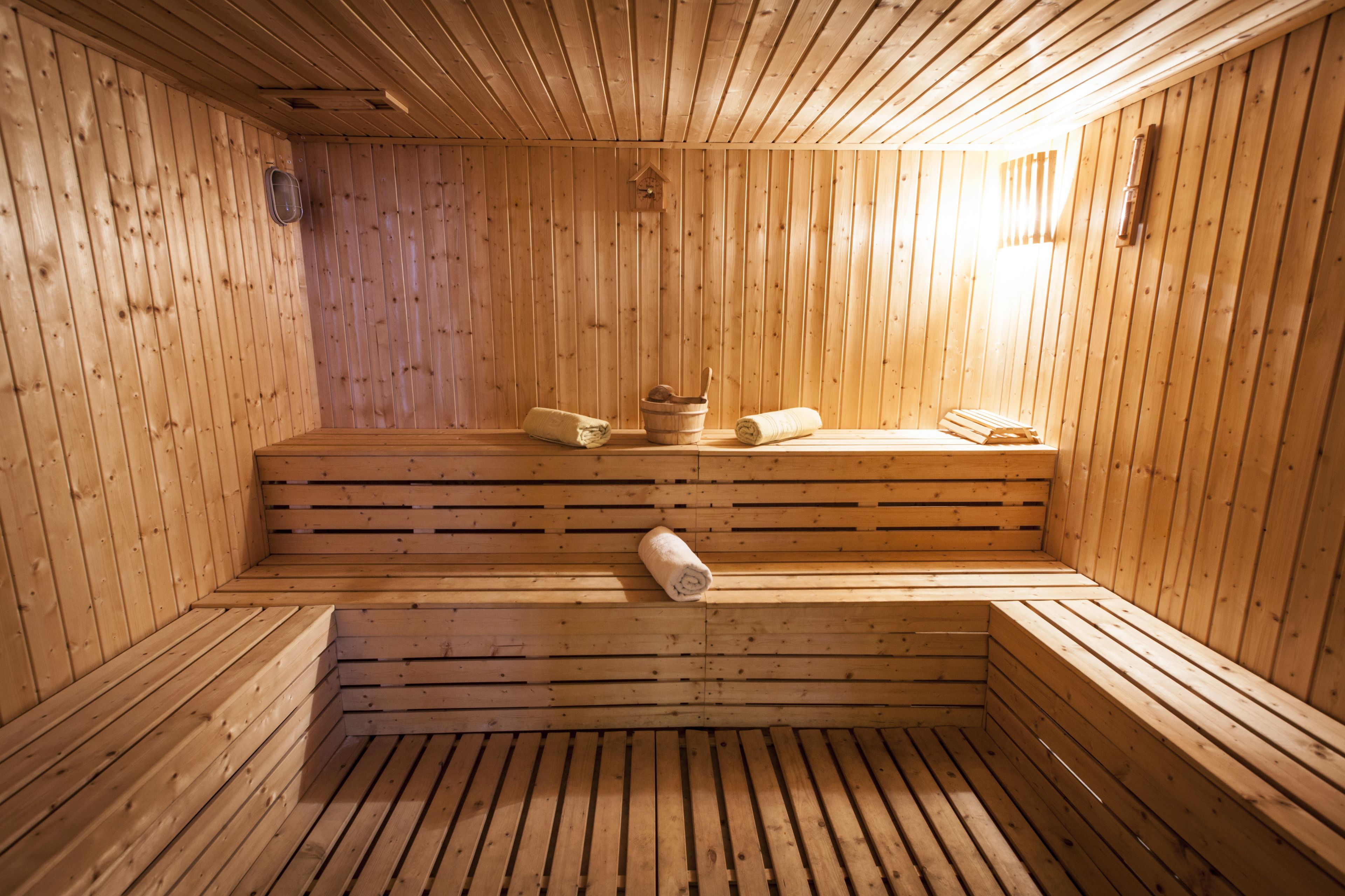 Una sauna con paredes y bancos de madera, un calentador para los bancos y un cubo.
