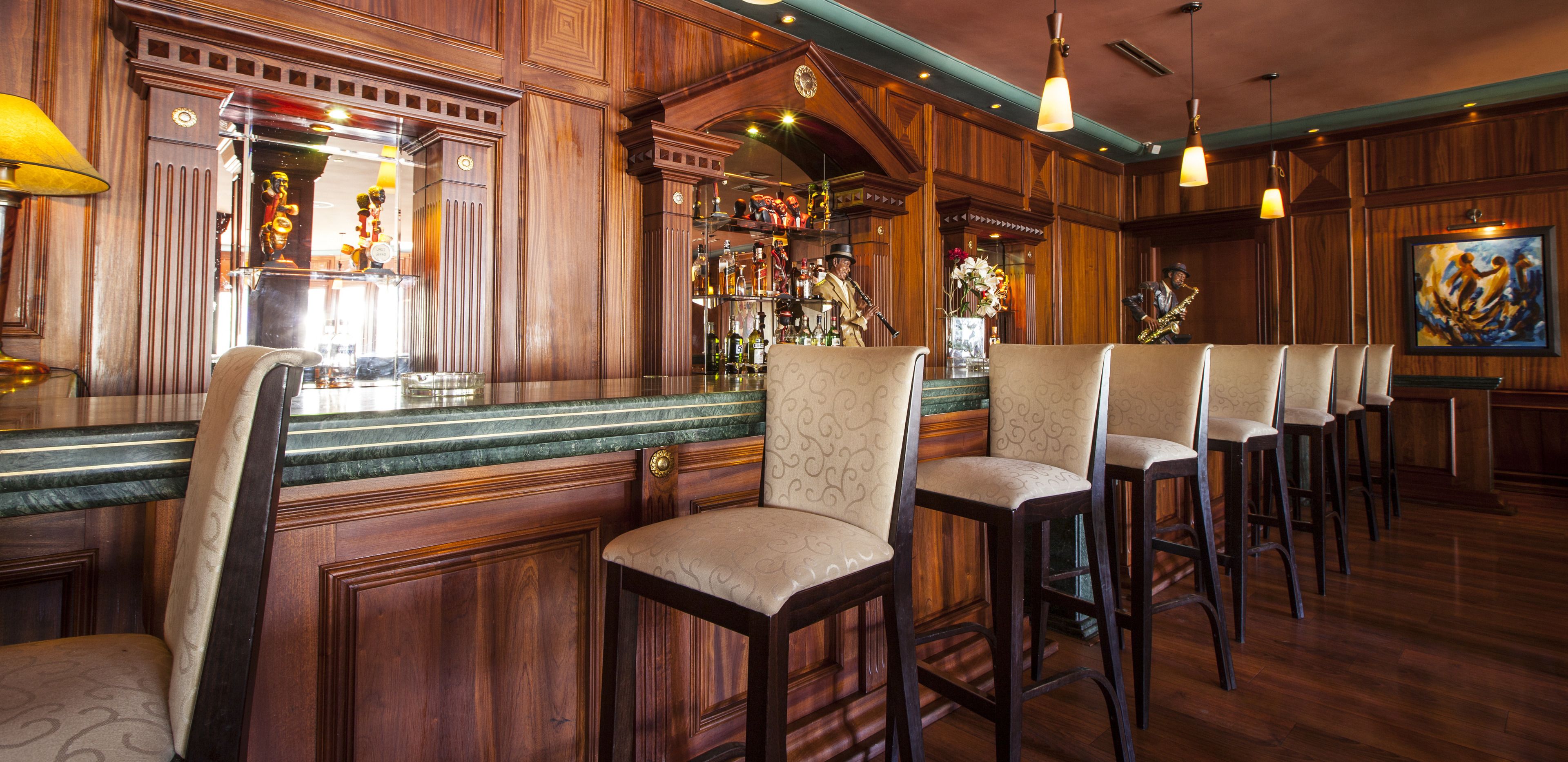 Zona de bar con paneles de madera, taburetes y una variedad de botellas y vasos en estanterías.
