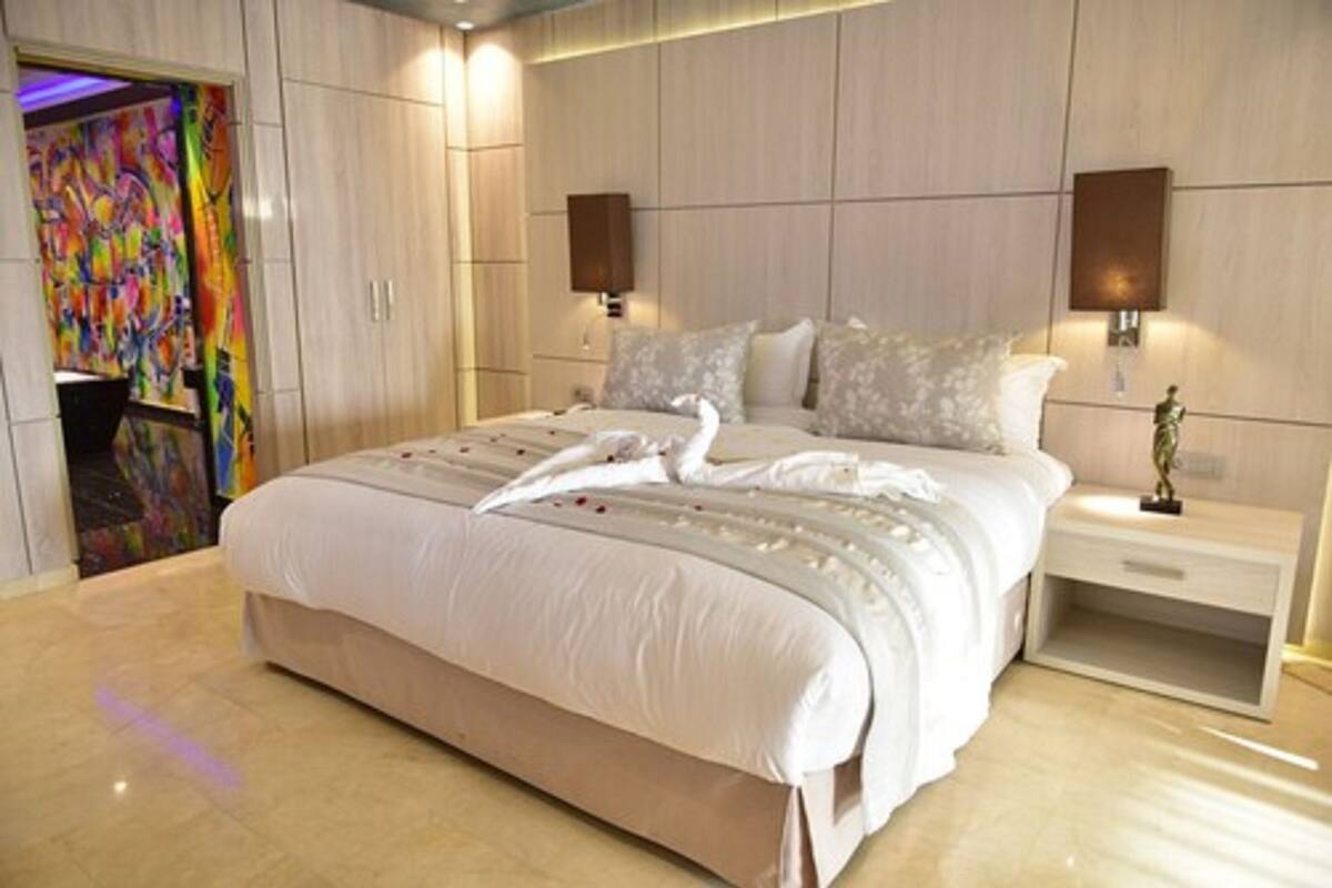 A modern hotel room with a large bed, a nightstand, and a wall-mounted lamp.