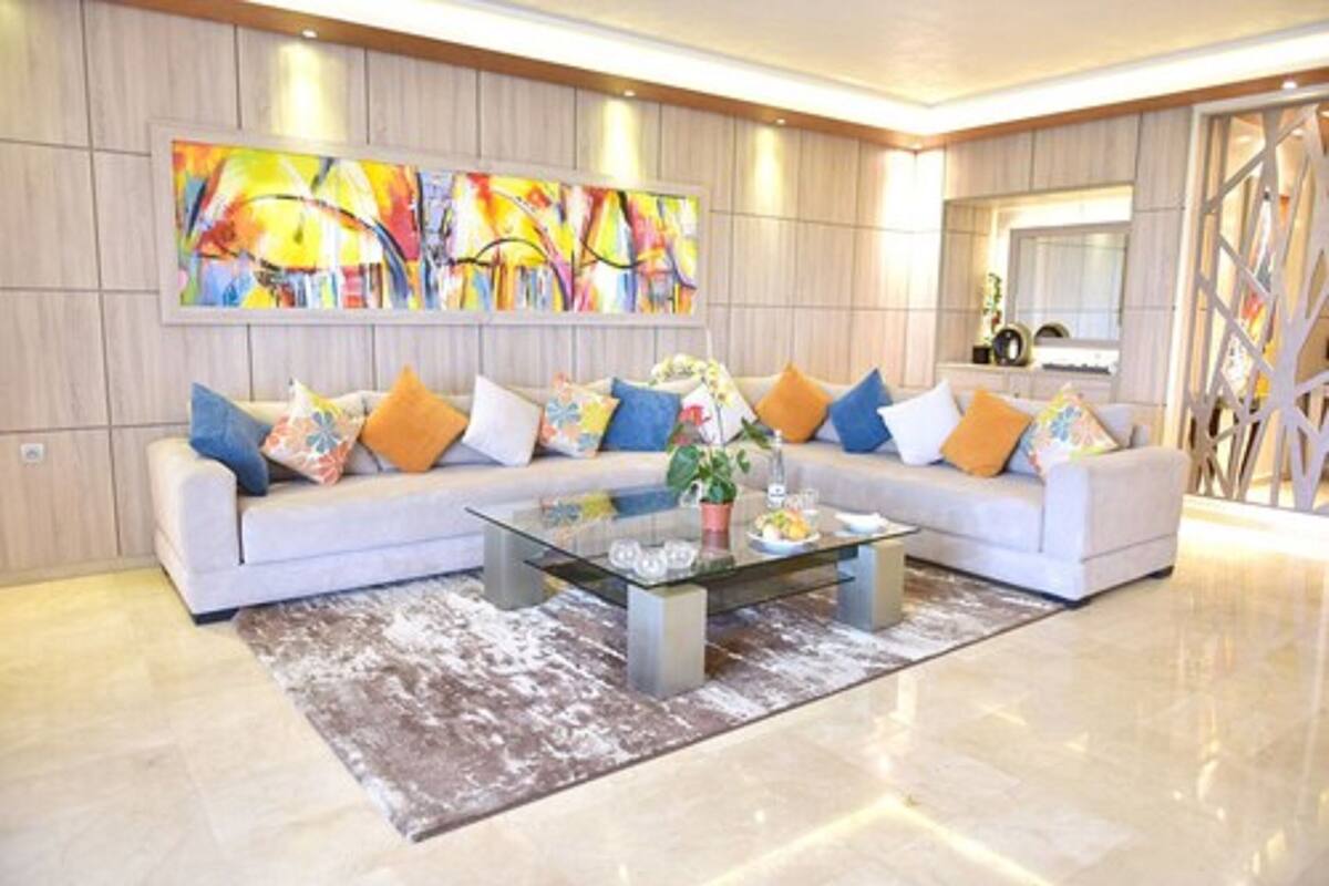 A modern living room with a sectional sofa, a glass coffee table, and a colorful abstract painting on the wall.