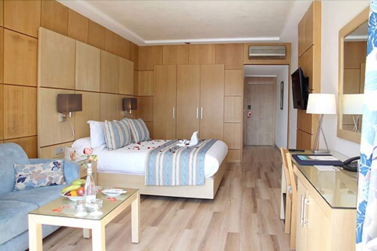 A hotel room with a bed, a sofa, a small table with a vase, and a TV on a cabinet.
