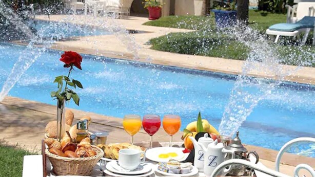 A breakfast tray with croissants, fruit, and juice by a pool with water jets. - Zaki Hotel  (Meknes)