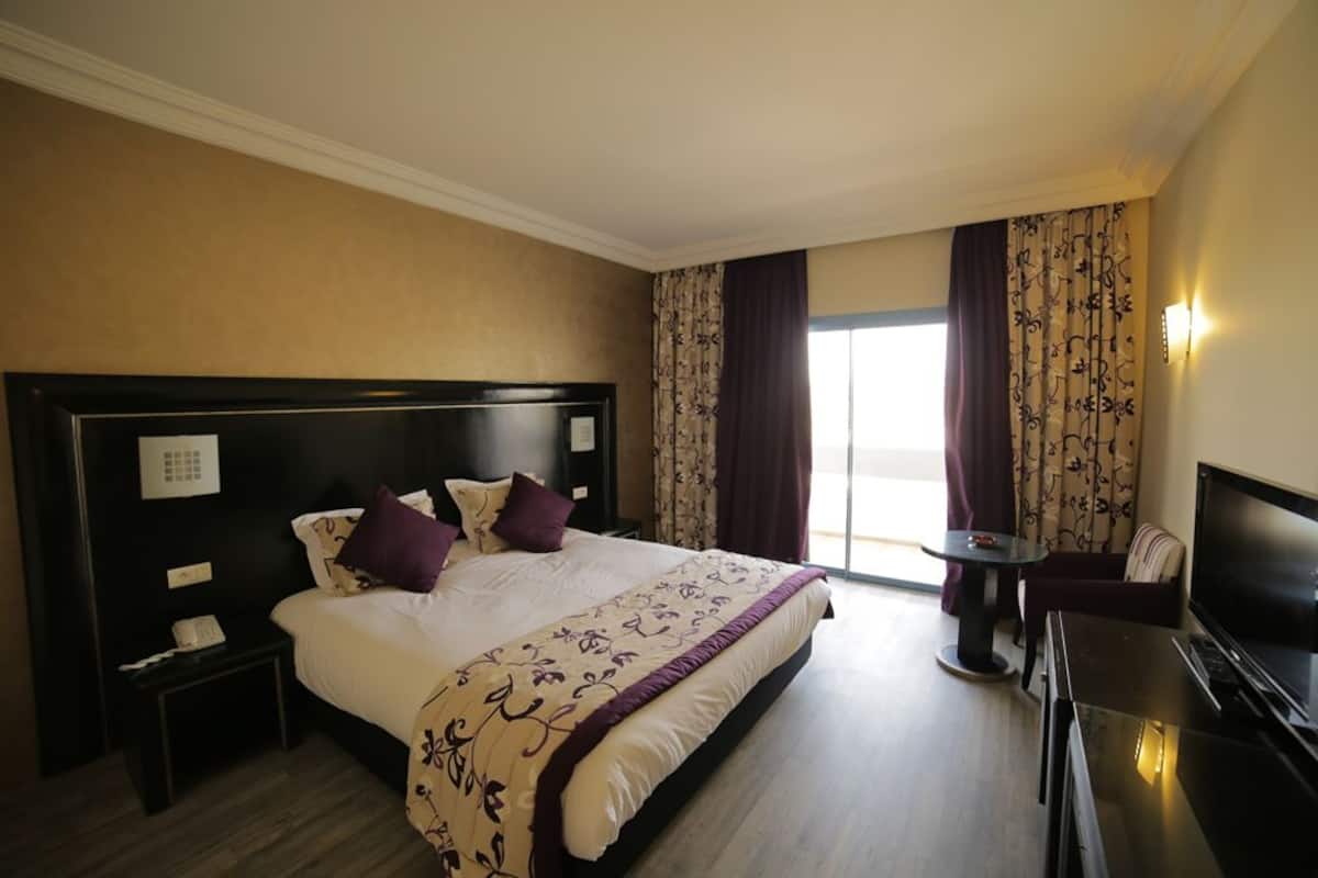 Habitación de hotel con una cama grande, una mesita de noche con teléfono, una pequeña mesa con una silla y una televisión.