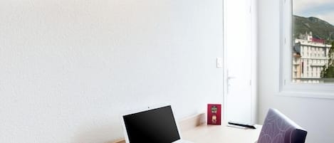A laptop on a desk by a window with a view of buildings and mountains.