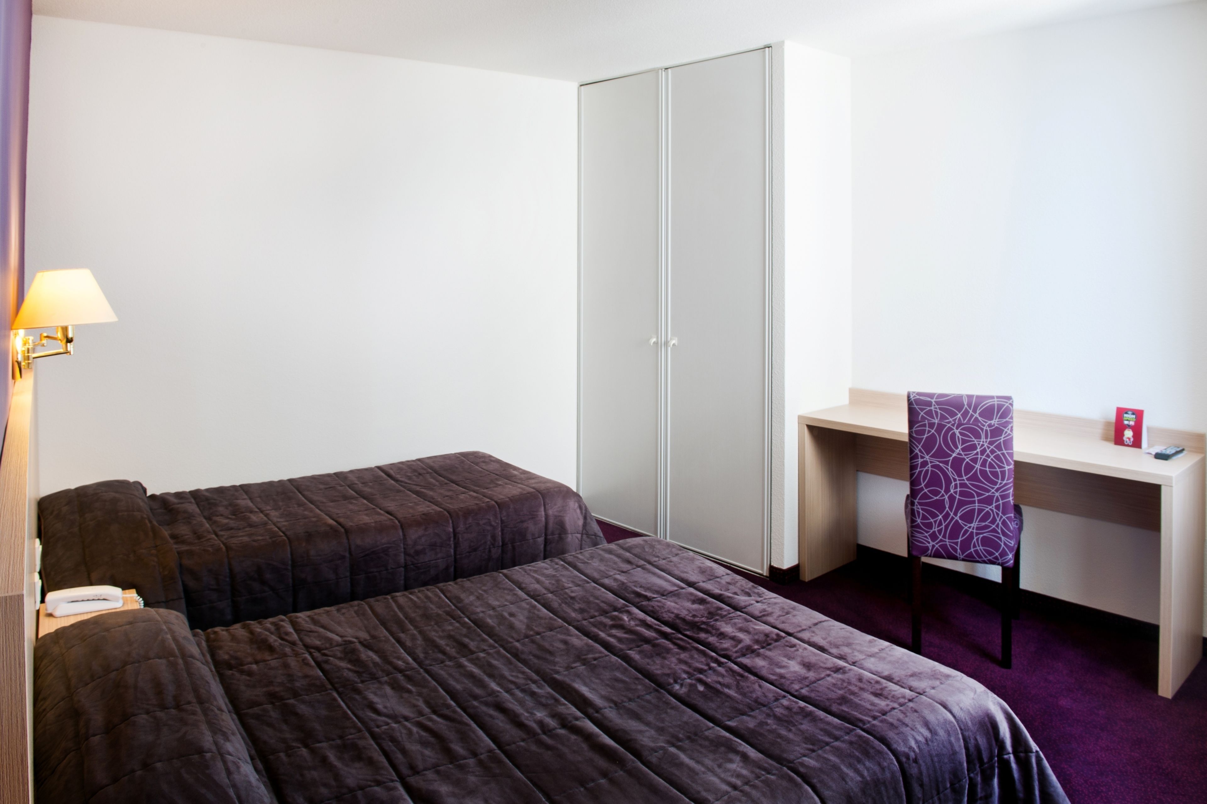 Una habitación de hotel con dos camas, un escritorio, una silla, un armario y una lámpara.