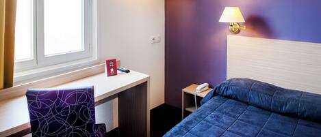 Una habitación de hotel con una cama, un escritorio con una silla, un televisor montado en la pared y dos lámparas de pared.
