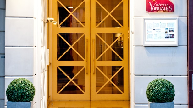 The entrance to Hotel Continental with a double door, a red fire alarm, and two potted plants. - Hotel Continental (Lourdes)