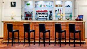 A bar area with a wooden counter, black bar stools, and shelves with various bottles and glasses. - Hotel Continental (Lourdes)