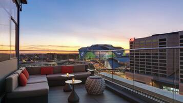 A modern rooftop lounge with a sofa, two small tables, and a patterned ottoman.