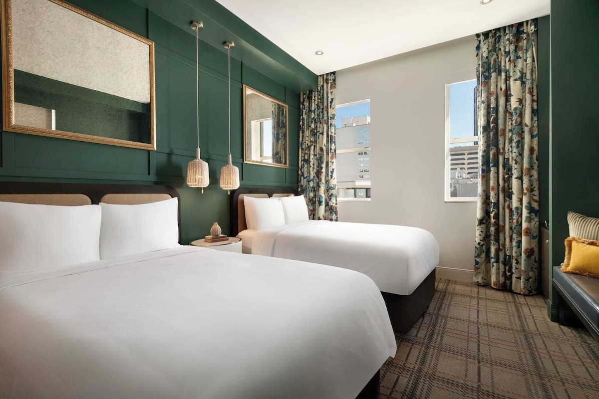 Habitación de hotel con dos camas, un espejo grande y vista a la ciudad.