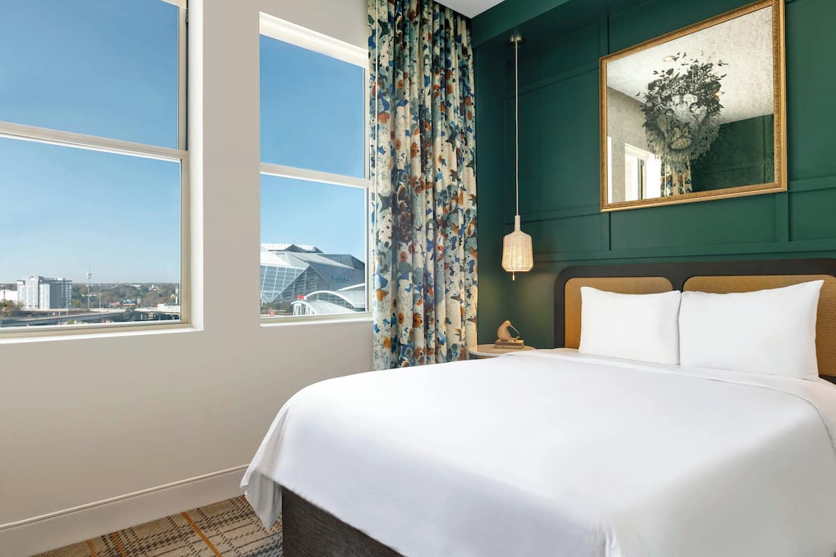 Habitación de hotel con una cama grande, vistas a la ciudad, un espejo y una ventana con cortinas.