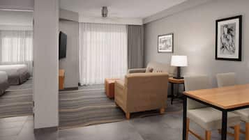 A modern hotel room with a bed, a sofa, a table, and a TV.