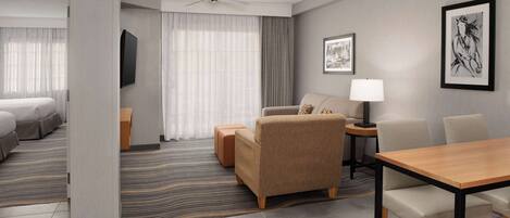 A modern hotel room with a bed, a sofa, a table, and a TV.