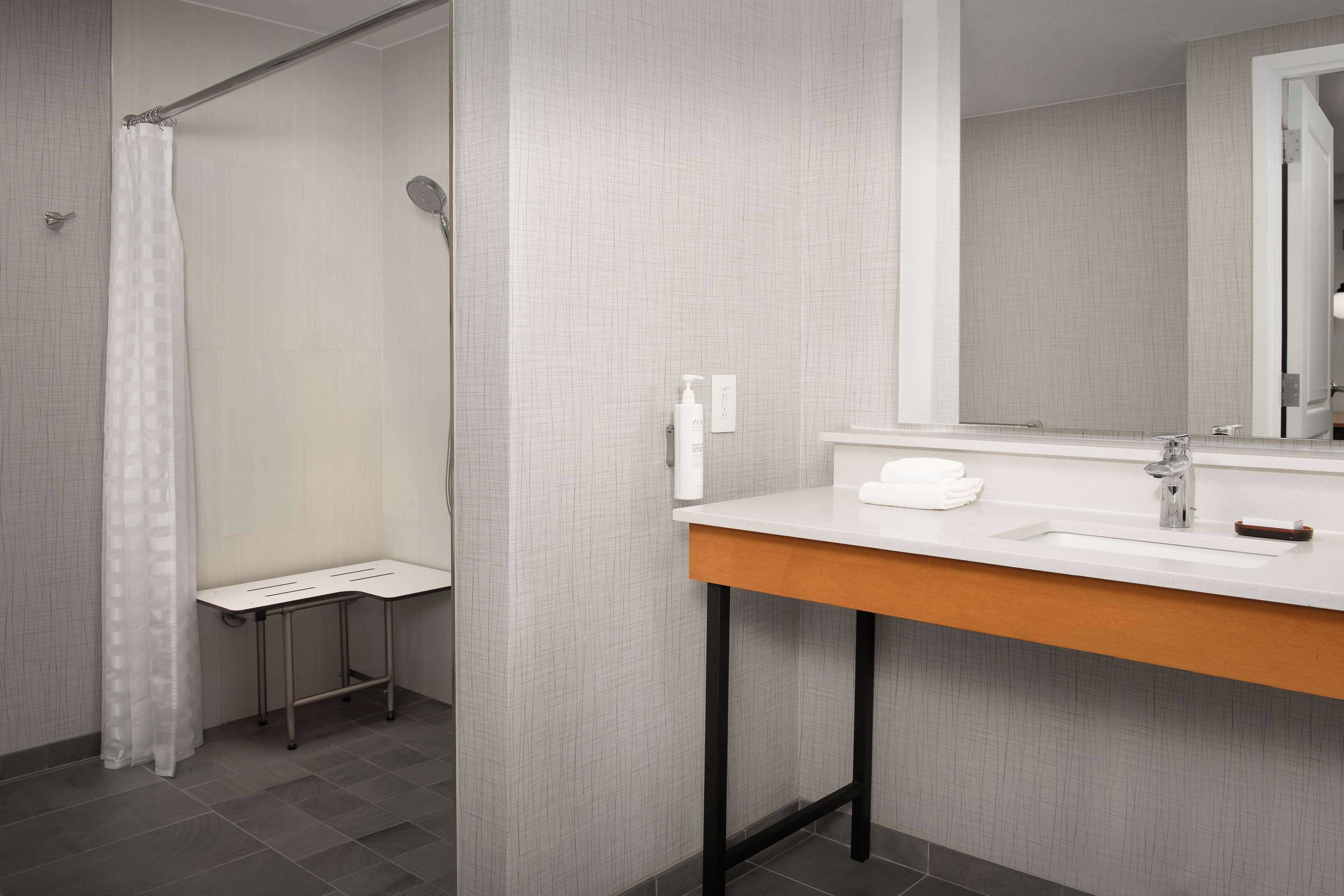 Un bany modern amb dutxa, un lavabo amb mirall i una taula petita.