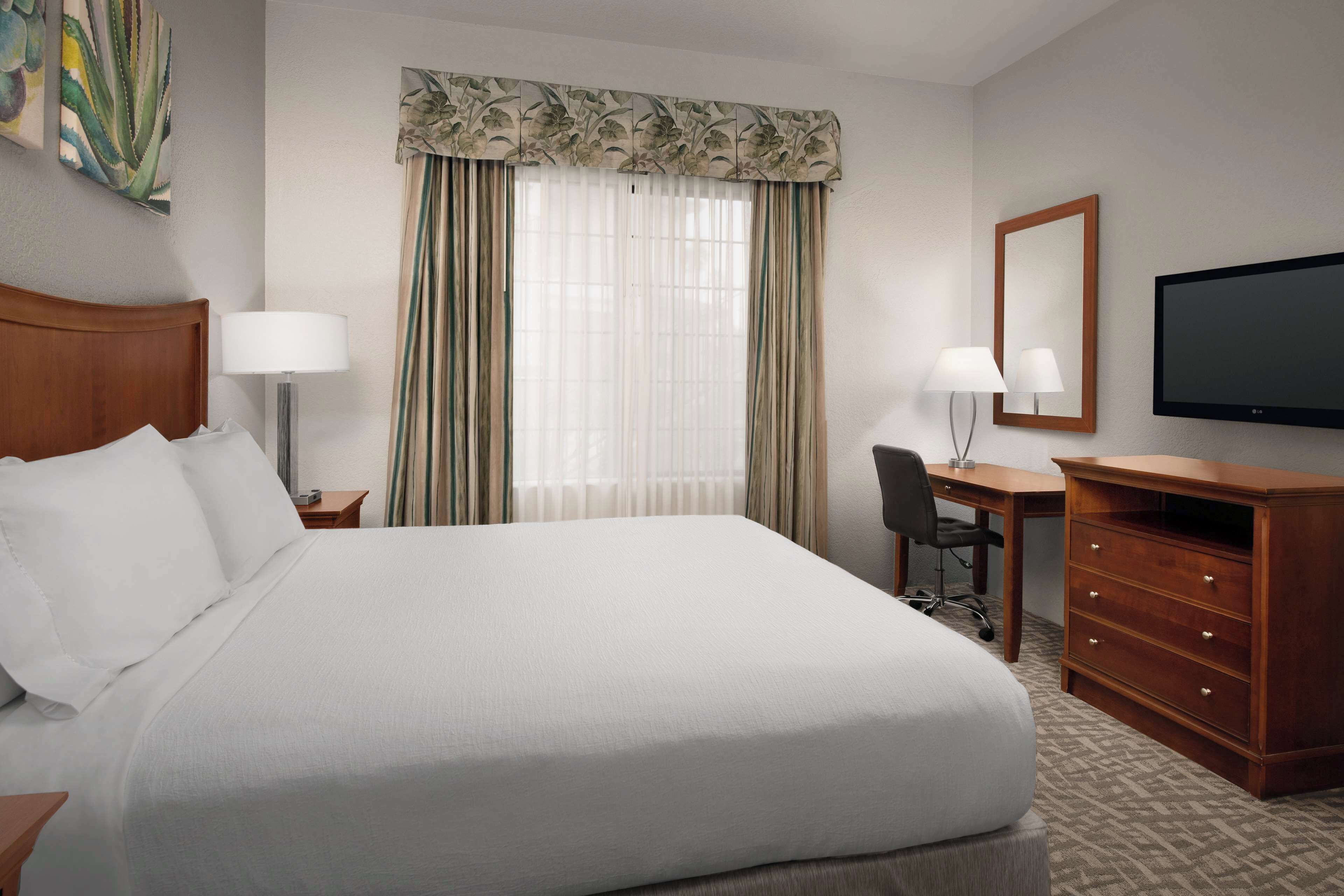 A hotel room with a large bed, a desk with a chair, a television, and a window with curtains.